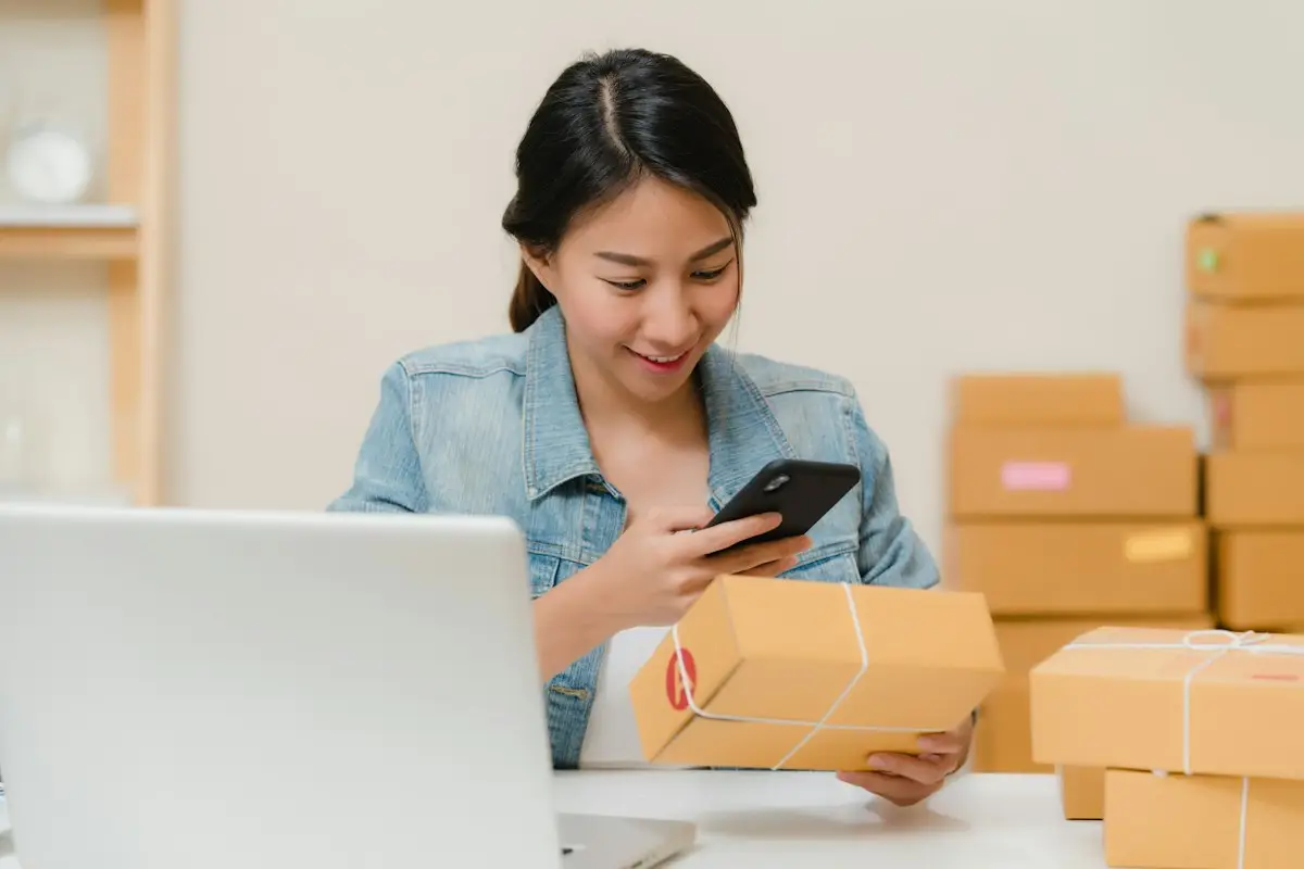 Small business owner scanning a package with her phone beside a laptop and boxes