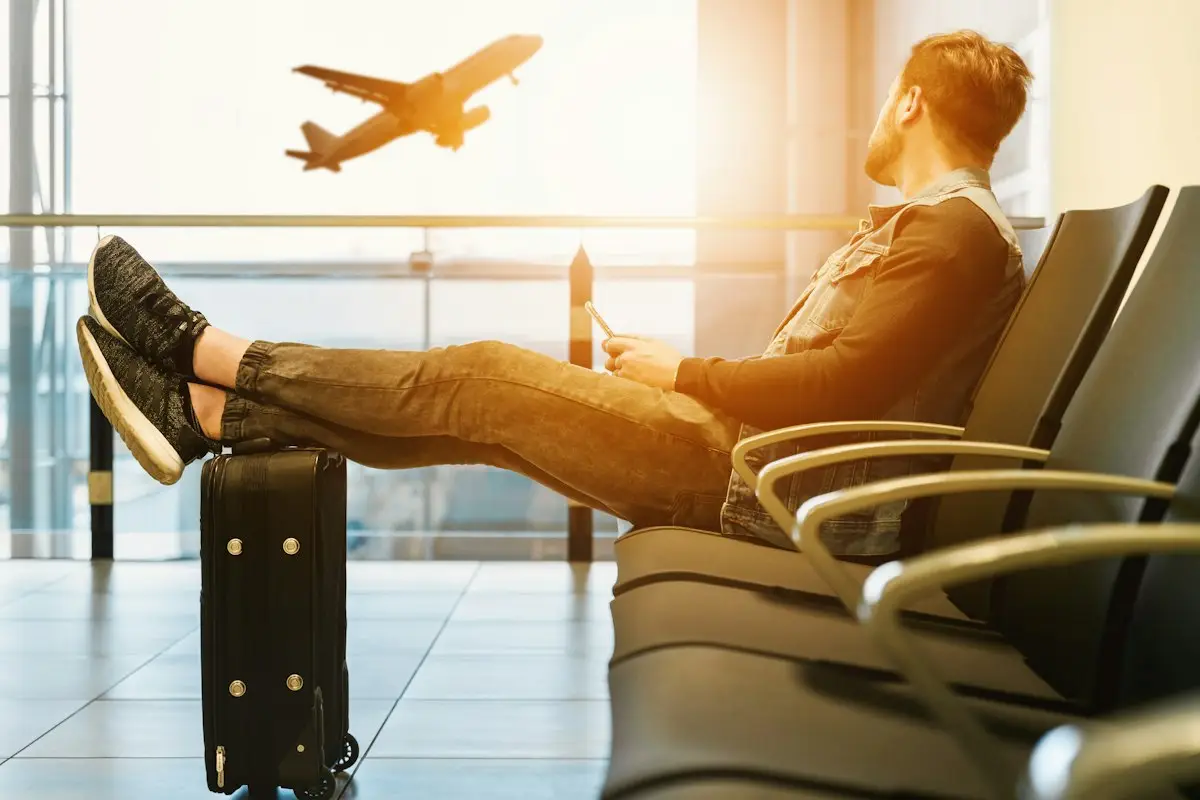 Traveller in an airport chair with feet on luggage watching a plane